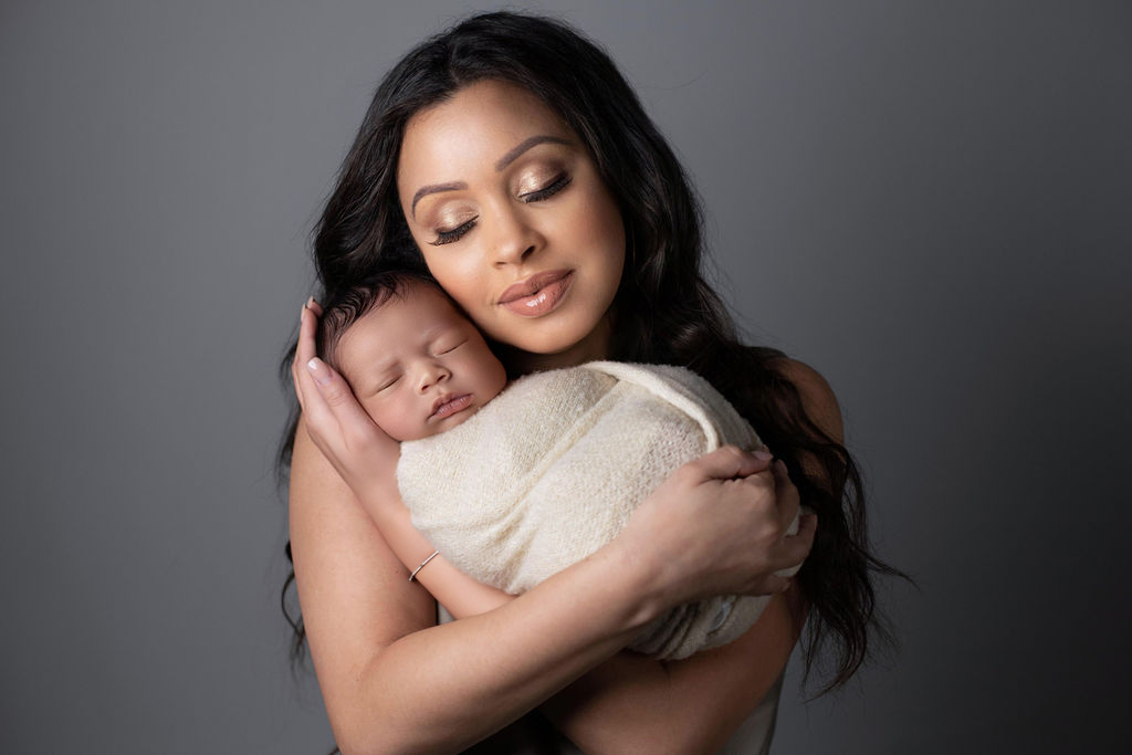 A San Antonio mother holds her newborn son cheek to cheek inside the studio, both wrapped in cream knit.