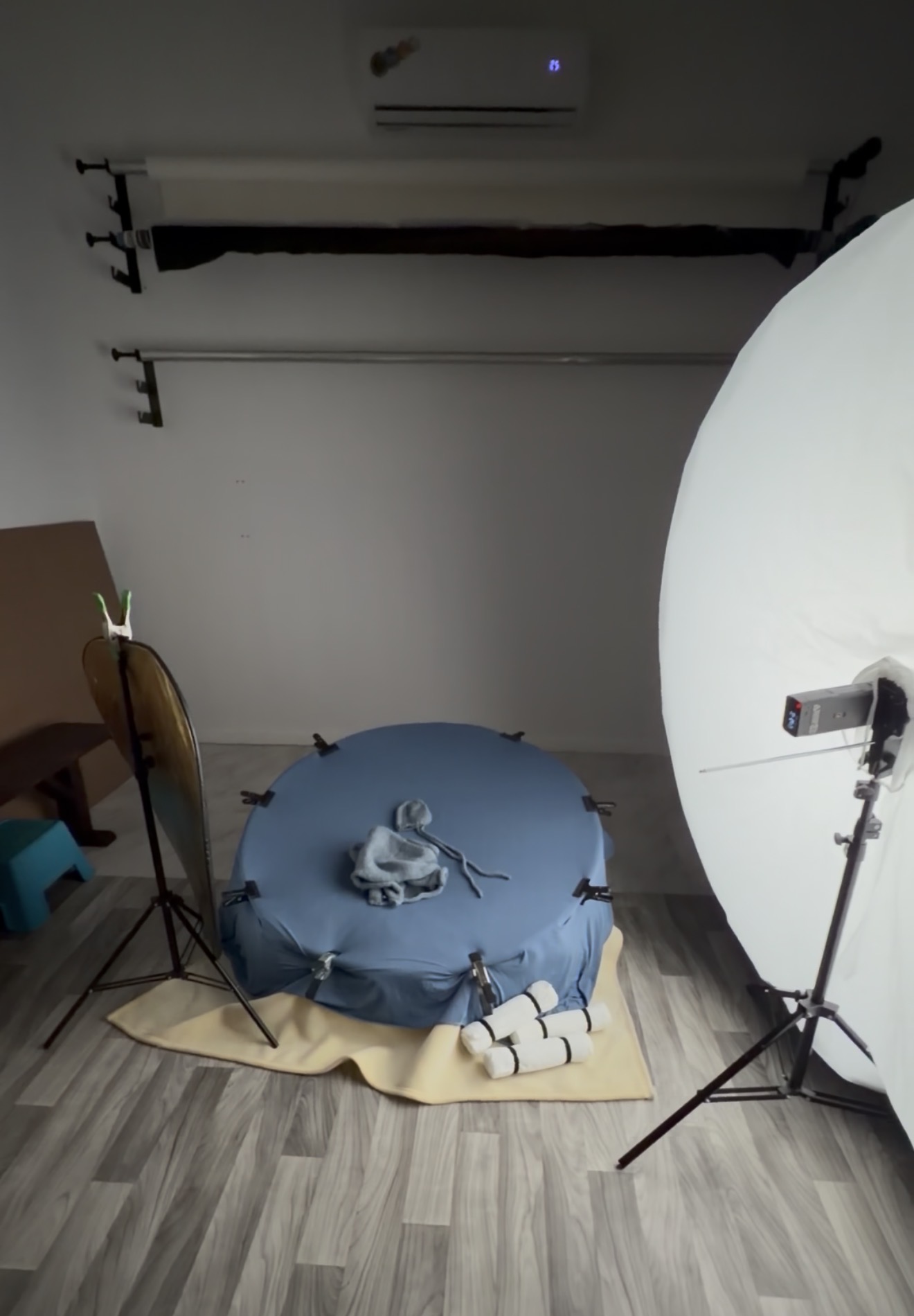 The Studio Realms newborn and maternity studio in San Antonio: backdrop bars, blue beanbag posing setup, large white reflector, professional softbox light, and warm hardwood floor.